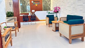 Un espace d’accueil comprenant un comptoir de réception, deux fauteuils en osier, un canapé vert et une petite table sur laquelle est posé un vase de fleurs.