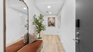 Un couloir avec un banc, un miroir, une plante et une porte.