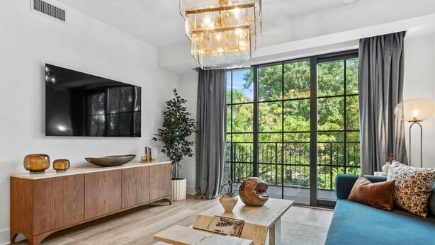 Un salon moderne avec une console en bois, une table basse, un canapé, un téléviseur fixé au mur et une grande fenêtre donnant sur un paysage verdoyant.