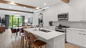 Une cuisine moderne avec des meubles blancs, un îlot central doté de tabourets, un four à micro-ondes encastré et une cuisinière.