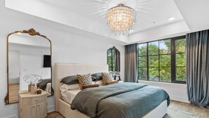 Une chambre à coucher avec un grand lit, un miroir, un lustre et une fenêtre avec des rideaux.