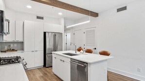 Une cuisine moderne avec des meubles blancs, des appareils en acier inoxydable et une poutre en bois au plafond.