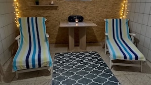Une pièce comprenant deux fauteuils à rayures, une petite table avec une bougie, un mur décoratif et une fenêtre ornée d’une statue de Bouddha.