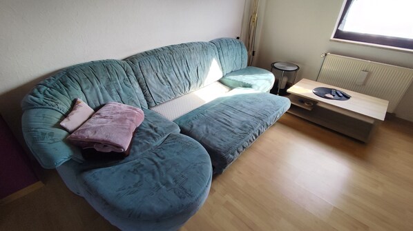 A living room with a teal sofa, a small round table with a remote control, and a radiator.