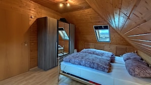 Une chambre avec un plafond en bois, un lit avec une literie à motifs, une armoire et un puits de lumière.