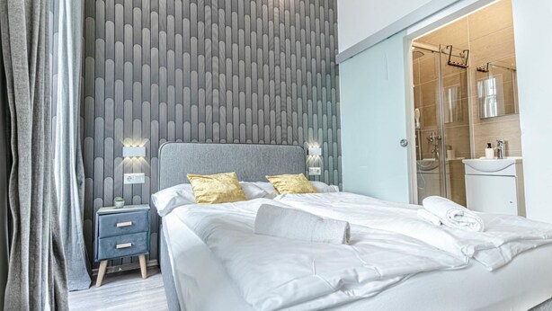 A modern hotel room with a large bed, bedside lamps, a nightstand, and a bathroom visible through an open door. - Beautiful Room, Wifi & TV, Near Mariahilferstraße (Vienna)