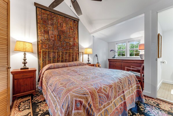 A bedroom with a large bed, two bedside tables with lamps, a dresser, a guitar, and a window with a view of greenery. - THE WRITER'S COTTAGE ~ Renovated Old Town 2 BR/2 Ba Home w/Parking! (Key West)