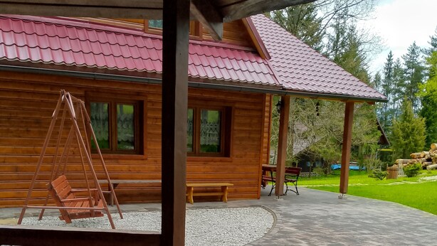 A wooden cabin with a red-tiled roof, a swing, a bench, and a patio area with stone tiles. - Chata Bobík (Oravice)