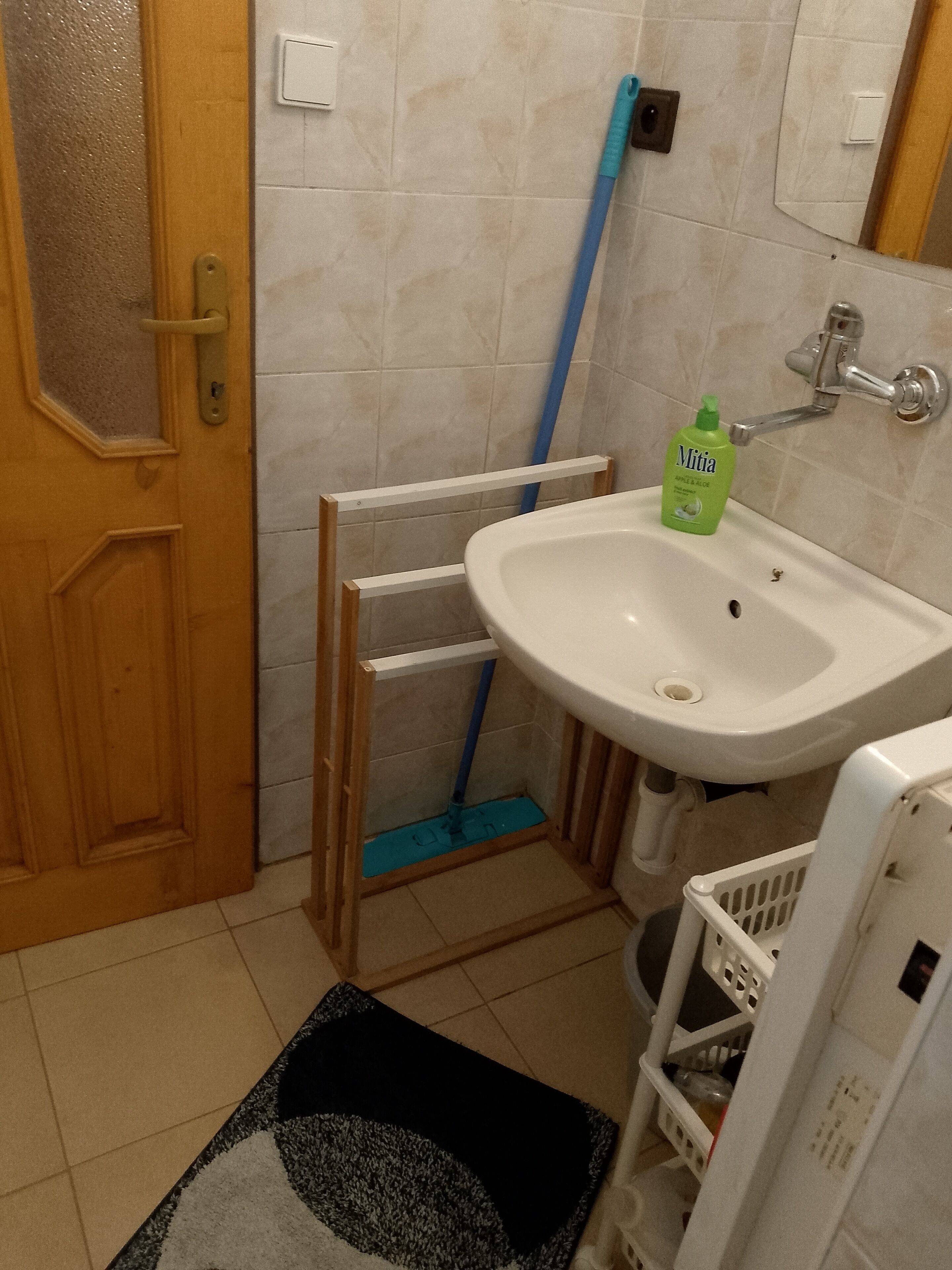 A bathroom with a white sink, a green bottle of Mitia, a blue mop, and a wooden door.