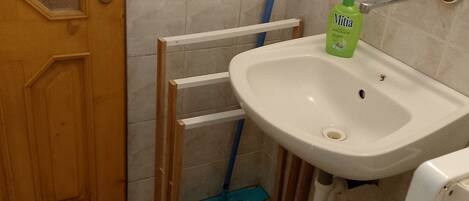 A bathroom with a white sink, a green bottle of Mitia, a blue mop, and a wooden door.