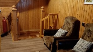 A cozy room with wooden walls, a patterned rug, two armchairs with cushions, a wooden chair, and a fire extinguisher. - Chata Bobík (Oravice)