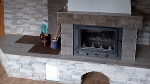 A stone fireplace with a white upper section, a small shelf, and a wooden shelf below. - Chata Bobík (Oravice)
