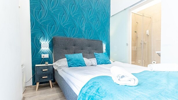 Une chambre à coucher avec un lit, une table de chevet, un mur orné d’un motif de feuilles et une porte en bois.