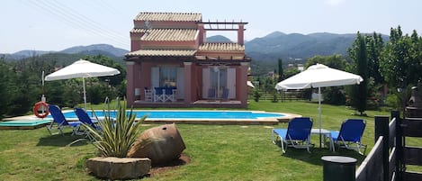 A villa with a swimming pool, outdoor seating, and a mountainous backdrop.