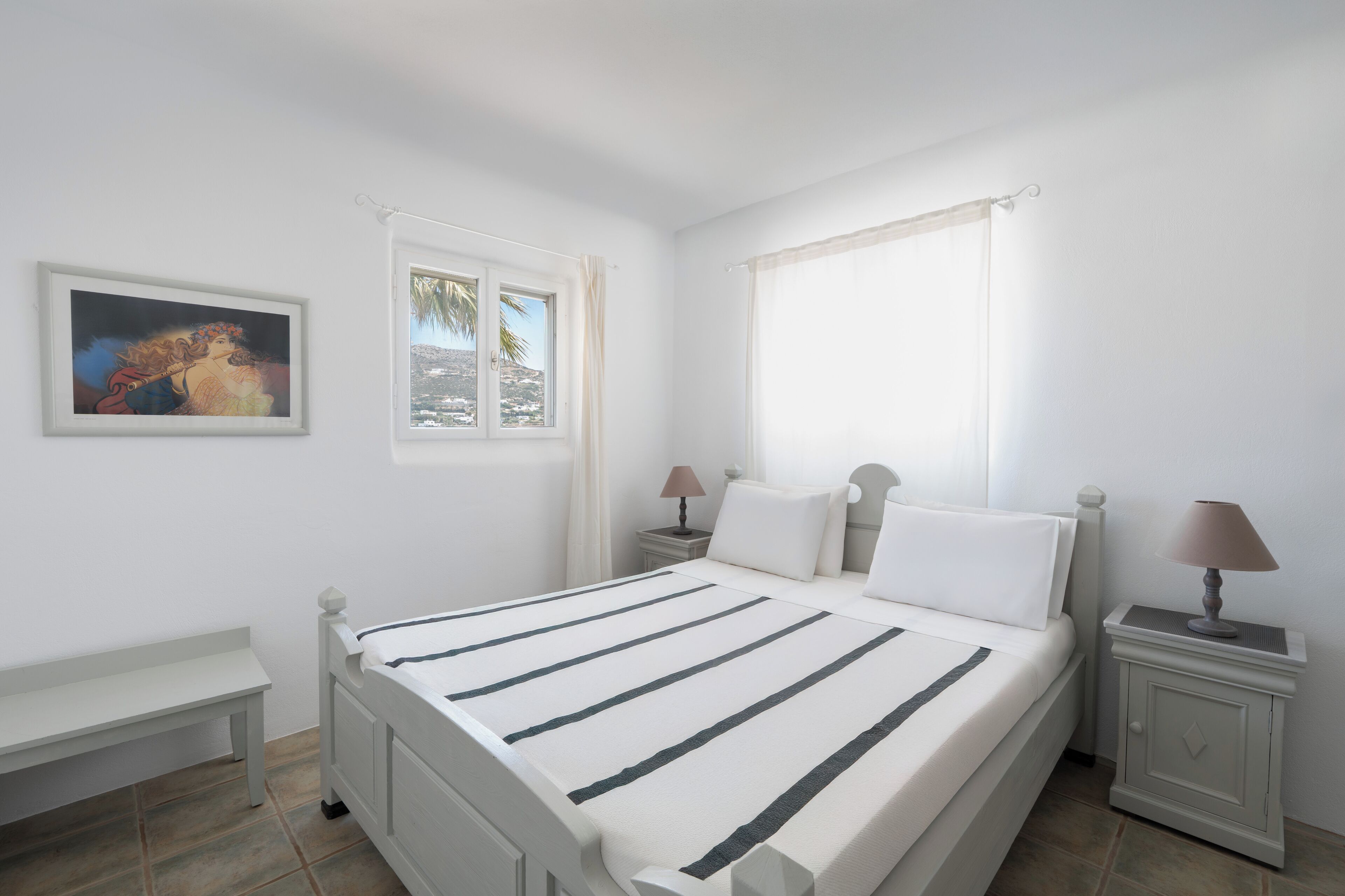 Ein Schlafzimmer mit einem Bett, zwei Nachttischen, einem Fenster mit Vorhängen und einem Wandbild.