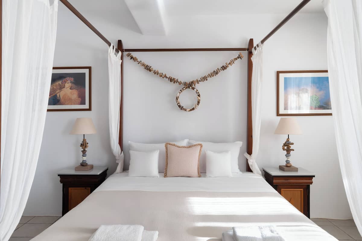 A four-poster bed with white linens, two bedside tables with lamps, and framed artwork on the walls.