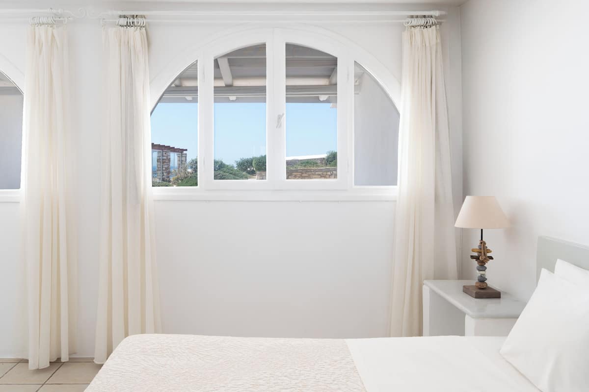 A bedroom with a large bed, a nightstand with a lamp, and a window with curtains.