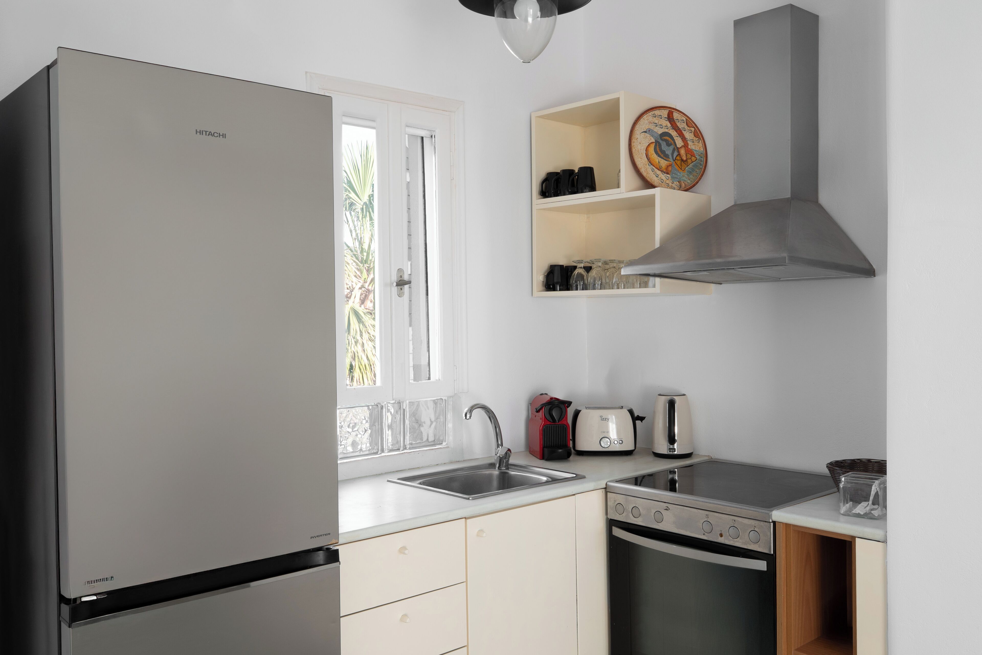 A modern kitchen with a refrigerator, sink, stove, and oven. There is a window with a view of greenery outside.