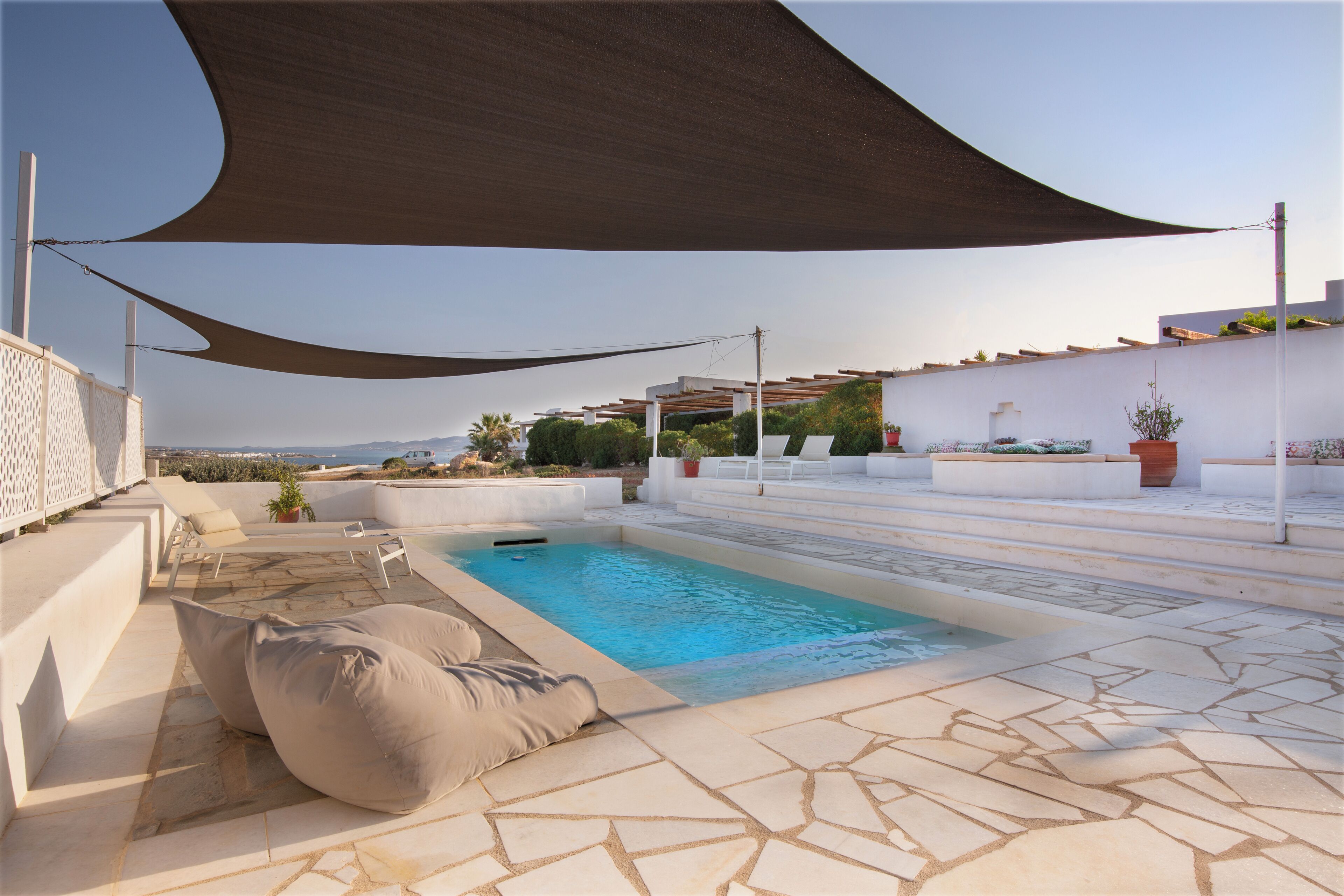 Una piscina en la azotea con suelo de piedra, rodeada de sillones de descanso y una gran vela de sombra.