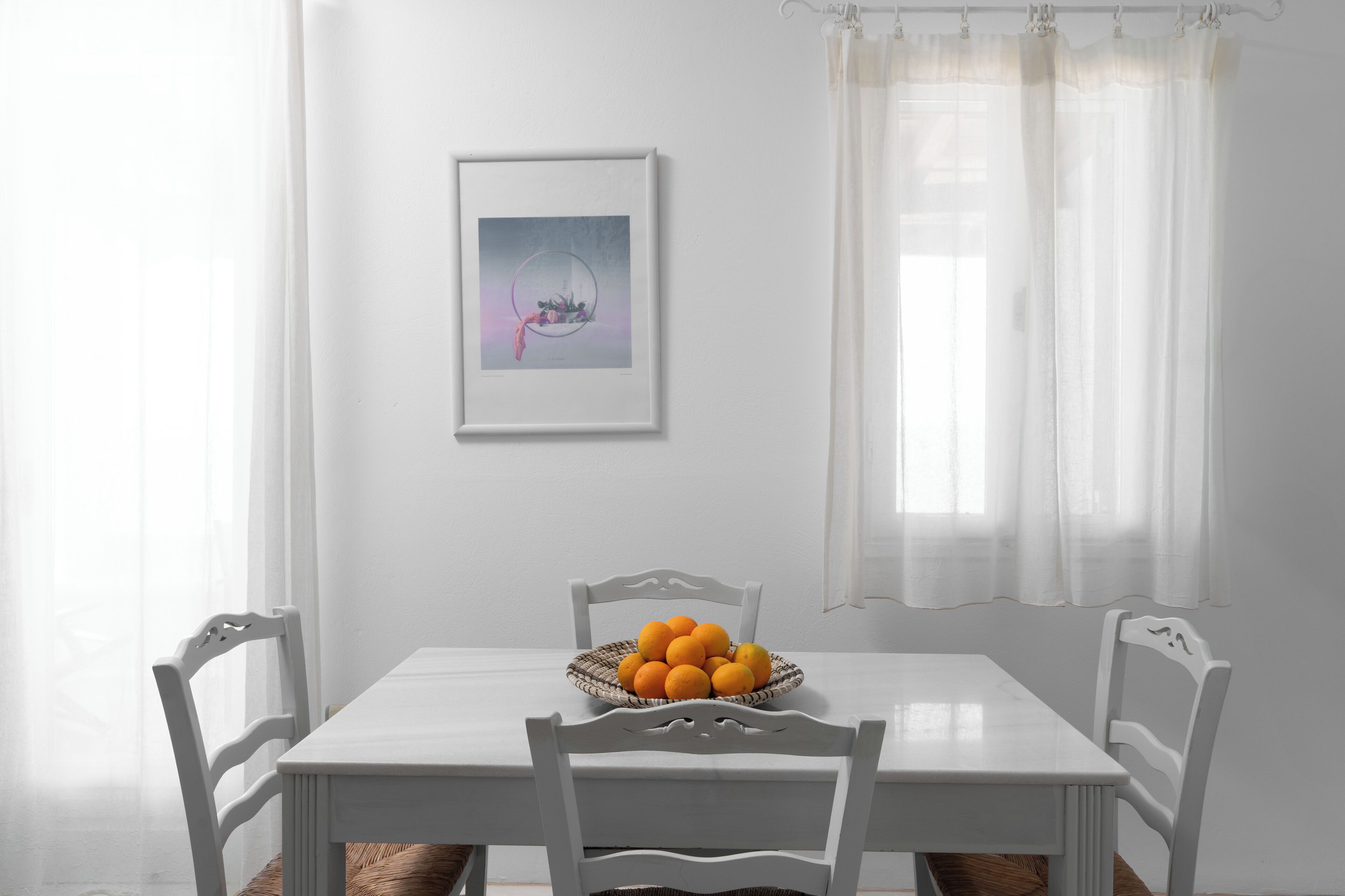 A dining table with a basket of oranges and white chairs.