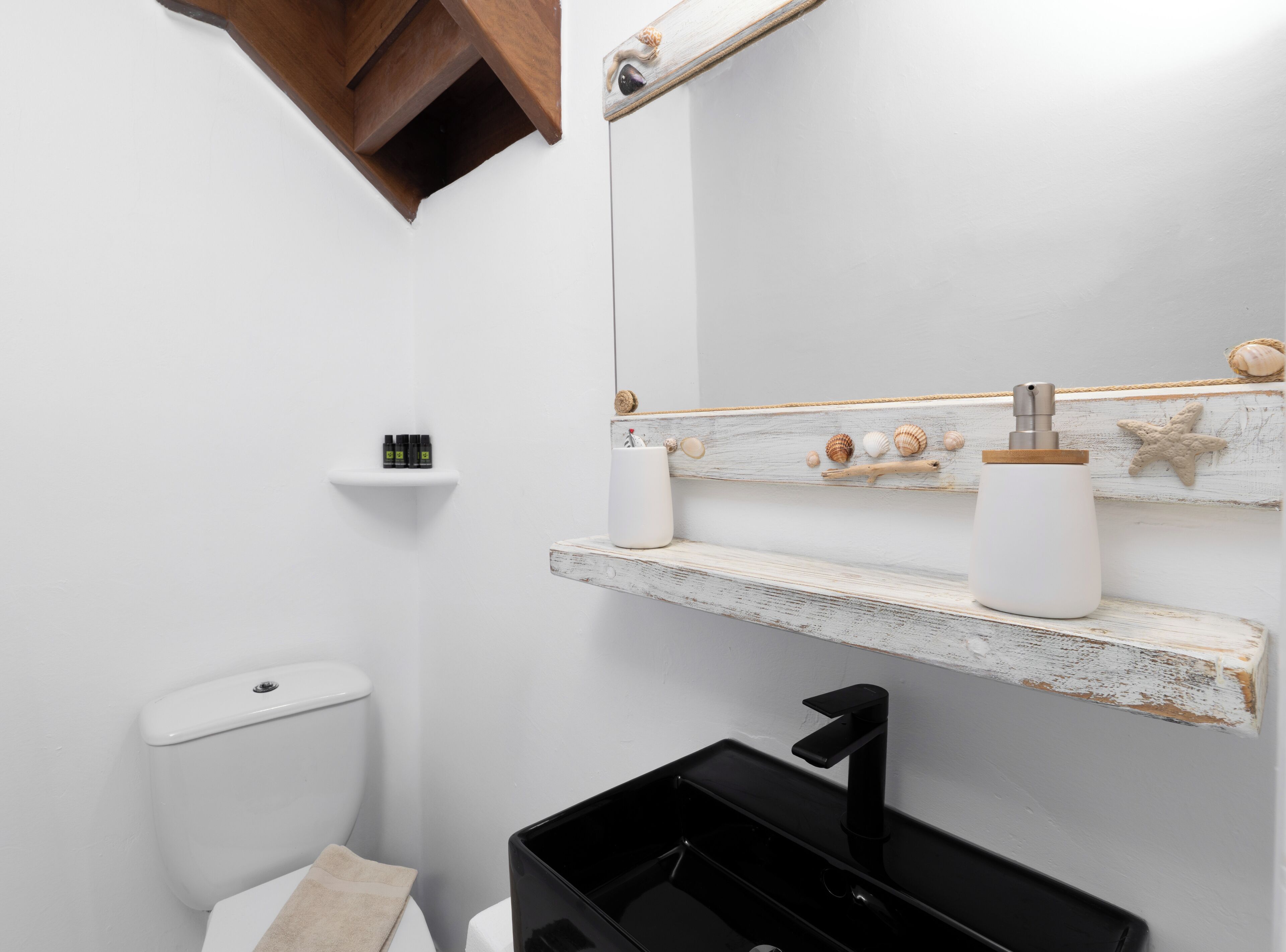A bathroom with a white toilet, a black sink, and a shelf with toiletries and decorative shells.