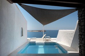 Una piscina con vista sul mare, una zona ombreggiata e un muro in pietra.