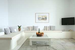 Ein Wohnzimmer mit einer Couch, einem Couchtisch mit Früchten, einem Gemälde und einem Fernseher.