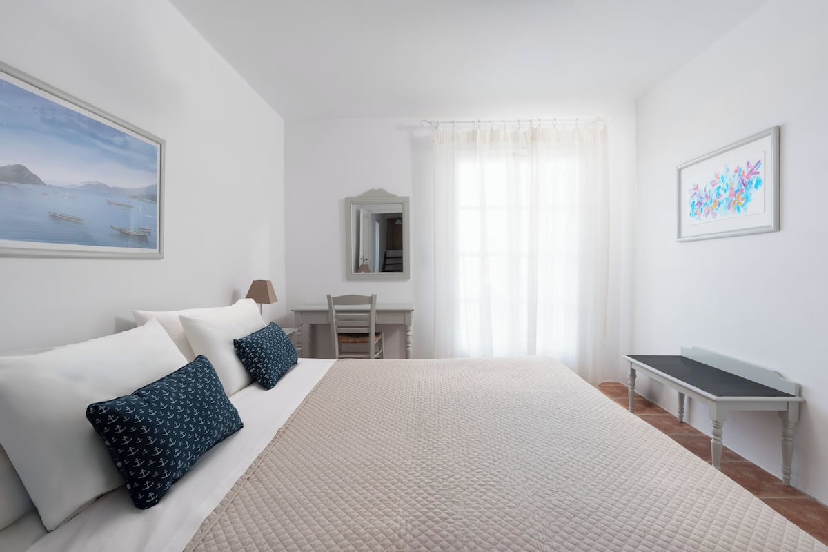 A hotel room with a large bed, a desk, a chair, and a small table.