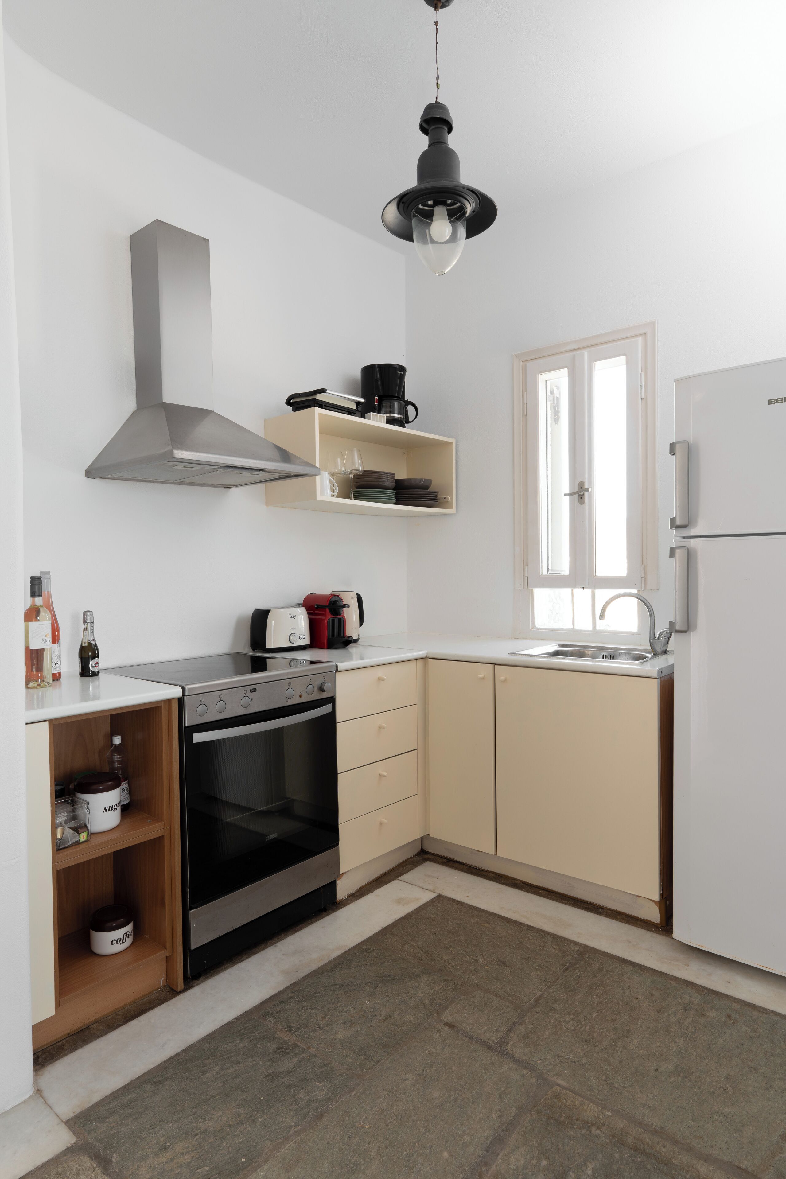 A compact kitchen with a stove, oven, and a built-in microwave. There is a sink, a window, and a hanging light fixture.