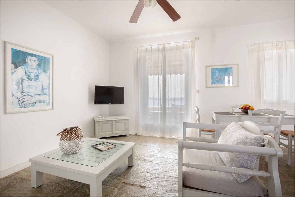 A bright, white room with a television, a dining table, and a sofa.