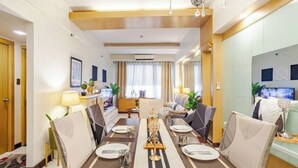 A modern dining area with a long table set for six, surrounded by upholstered chairs. - Stunning Suite 10 Steps from Eastwood Mall (Quezon City)