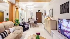 A modern living room with a sofa, a coffee table, a TV, and a dining area with a table and chairs. - Stunning Suite 10 Steps from Eastwood Mall (Quezon City)