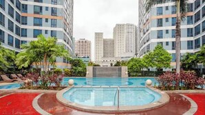 A swimming pool surrounded by palm trees and red flooring, with tall buildings in the background. - Stunning Suite 10 Steps from Eastwood Mall (Quezon City)