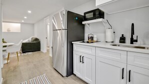 Ett modernt kök med vita skåp, ett kylskåp i rostfritt stål, en mikrovågsugn och en diskho.