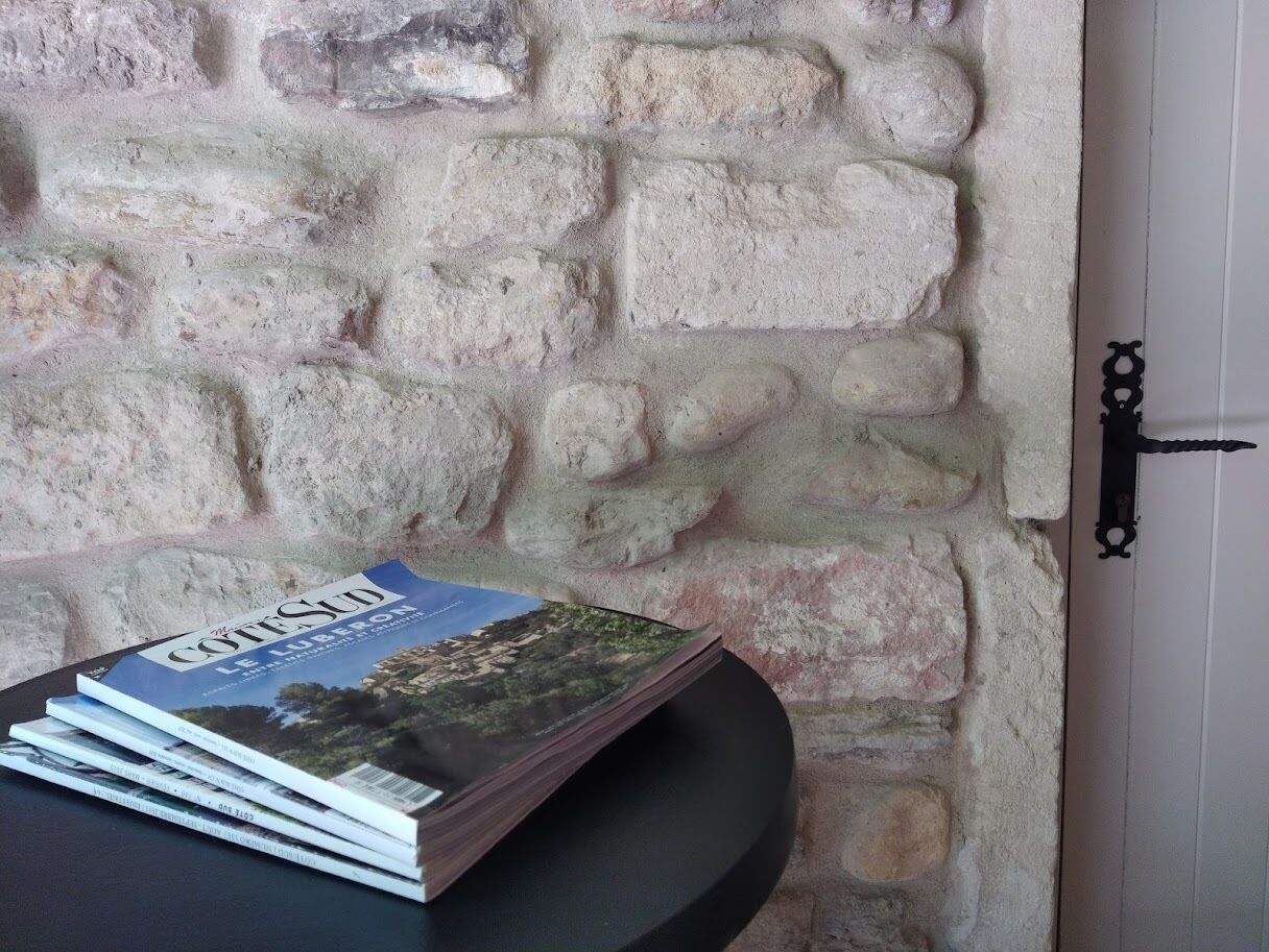 A stack of magazines on a table against a stone wall with a door.