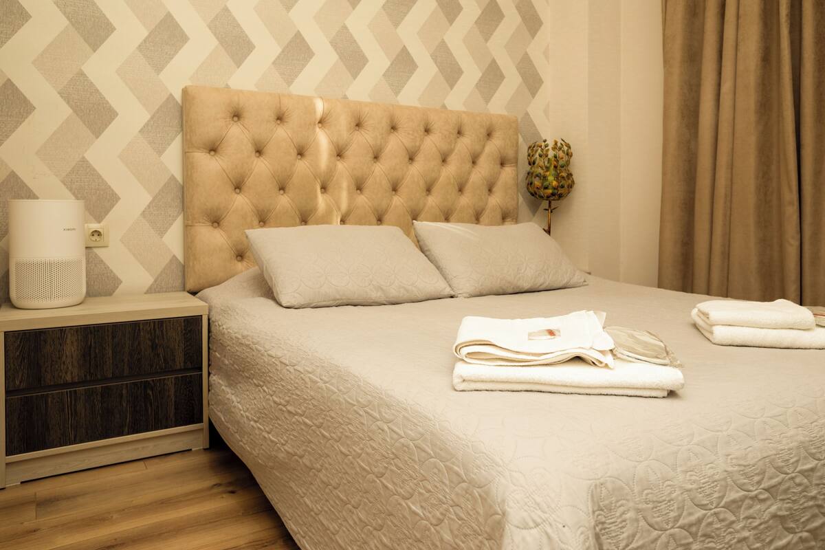 A neatly made bed with a tufted headboard, a bedside table with a lamp, and a wall with a geometric pattern.