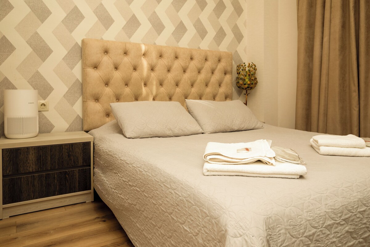 A neatly made bed with a tufted headboard, a bedside table with a lamp, and a wall with a geometric pattern.