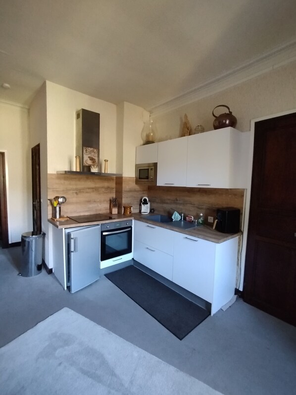 Una cocina compacta con armarios blancos, horno integrado, microondas y fregadero. Hay un pequeño cubo de basura y una alfombra en el suelo.