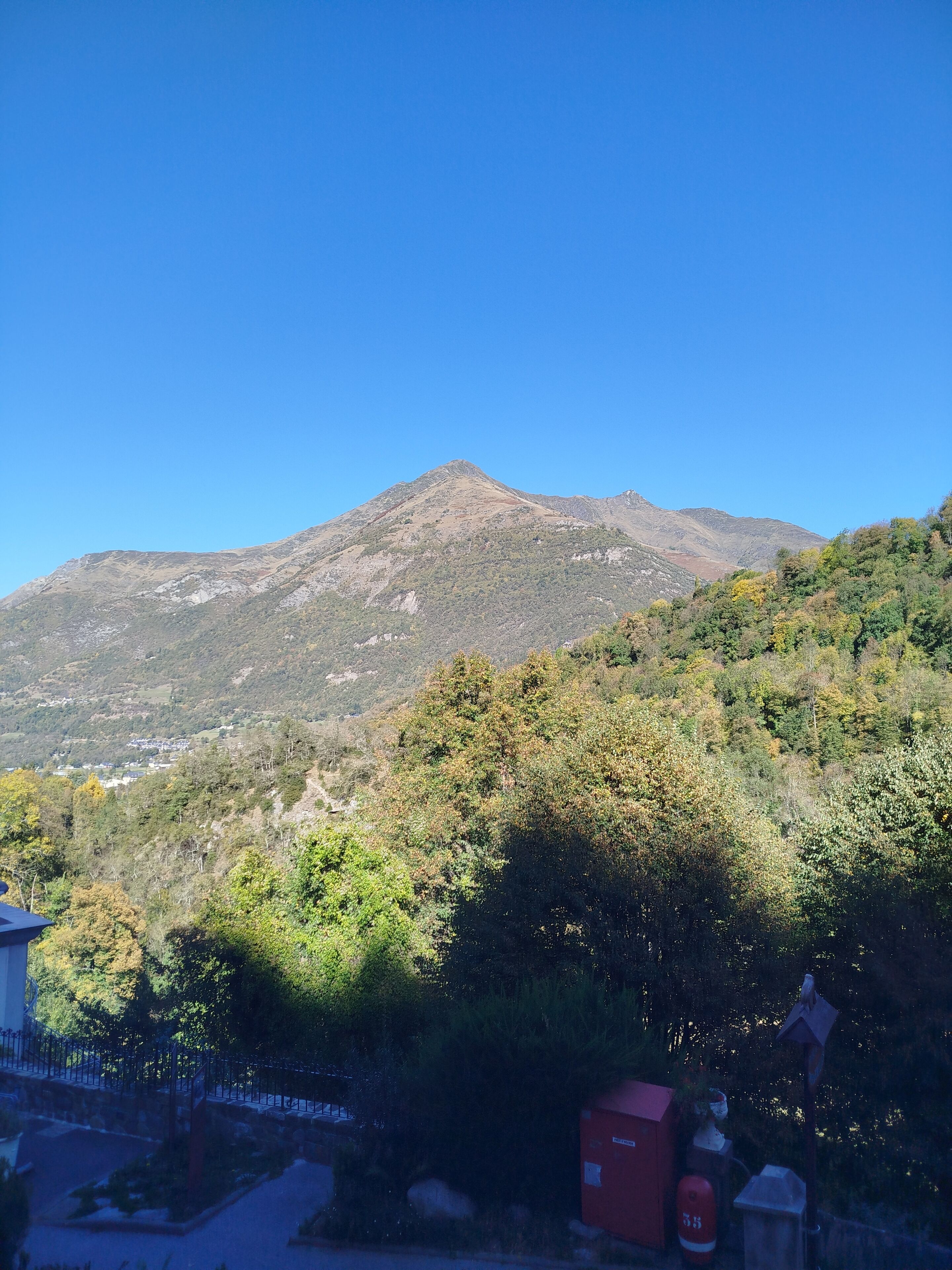 Montanha sob um céu limpo. Árvores e um edifício em primeiro plano.