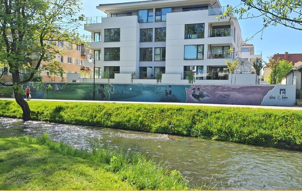 A modern building with multiple floors, a landscaped area with a water feature, and a mural on the side. - Apartment Zamkowa Park (Węgorzewo)