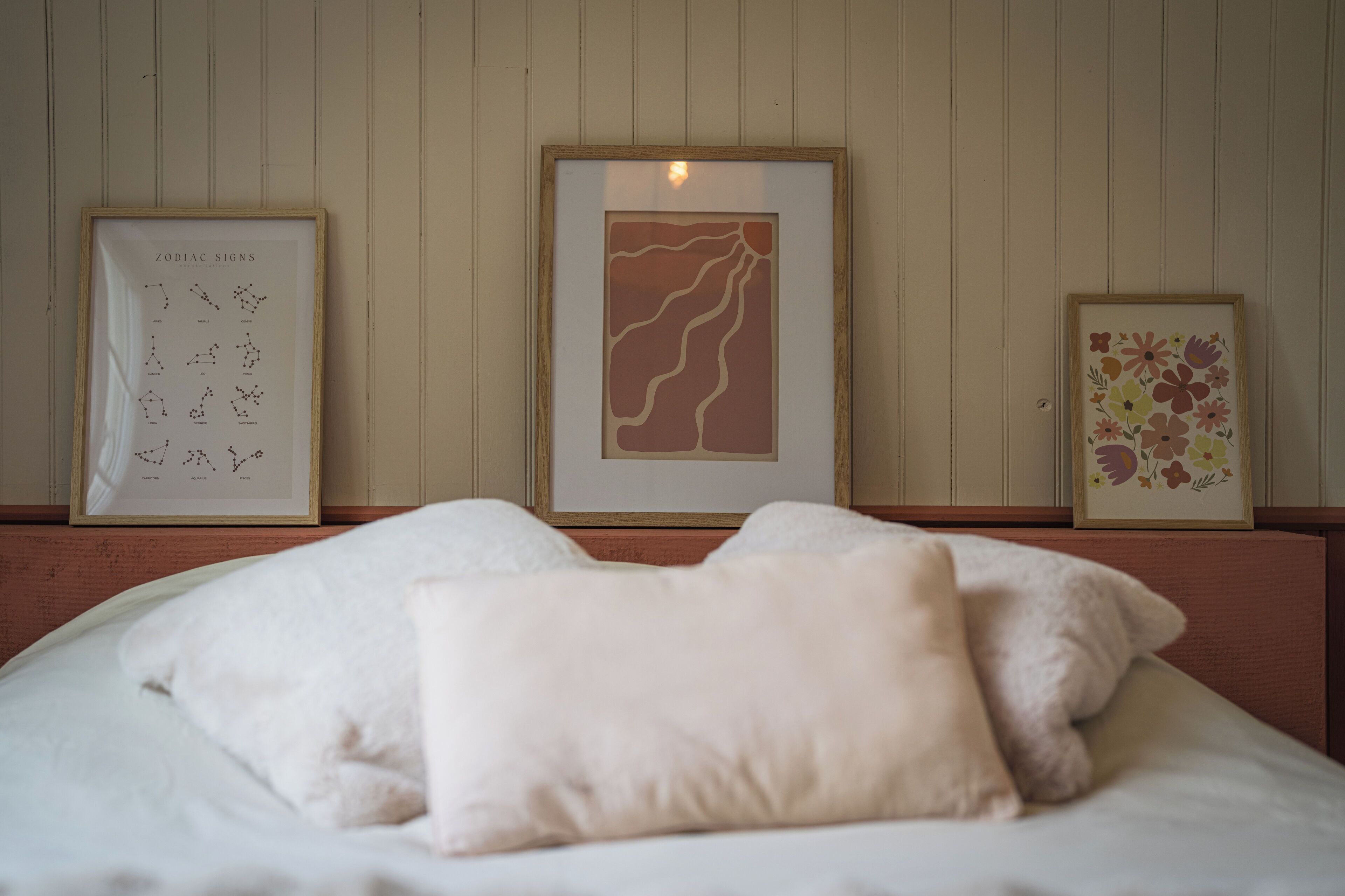 A bed with white bedding and a single beige pillow, framed artwork on the wall, and a wooden headboard.