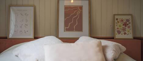 A bed with white bedding and a single beige pillow, framed artwork on the wall, and a wooden headboard.