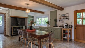 Una cocina amplia con una mesa y sillas de madera, una chimenea de ladrillo y un ventanal con vistas a la vegetación.