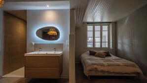 Un dormitorio moderno con suelo de madera, una cama grande con colcha color beige, una mesita de noche y una ventana con vistas al exterior.