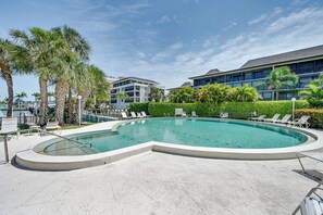 Une piscine à bords incurvés, entourée de chaises longues et de palmiers.