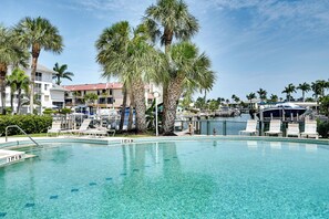 Une piscine aux eaux cristallines, bordée de chaises longues, de palmiers et avec une marina en arrière-plan.