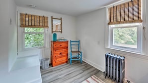 Ein Zimmer mit zwei Fenstern, einem Heizkörper, einem Holzschrank, einem blauen Stuhl und einem Spiegel an der Wand.