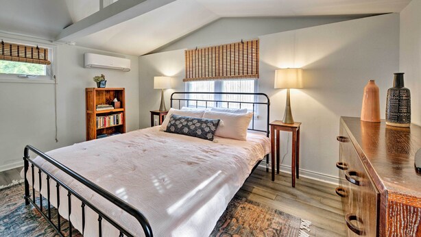 Ein Schlafzimmer mit Bett, Nachttischen, einem Bücherregal, einer Kommode und einem Fenster mit Jalousien.