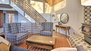A cozy living room with a wooden staircase, a fireplace, and a checkered sofa.