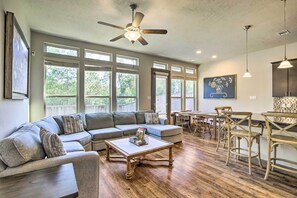 Un salon spacieux avec un canapé d’angle, une table basse en bois et un ventilateur de plafond.